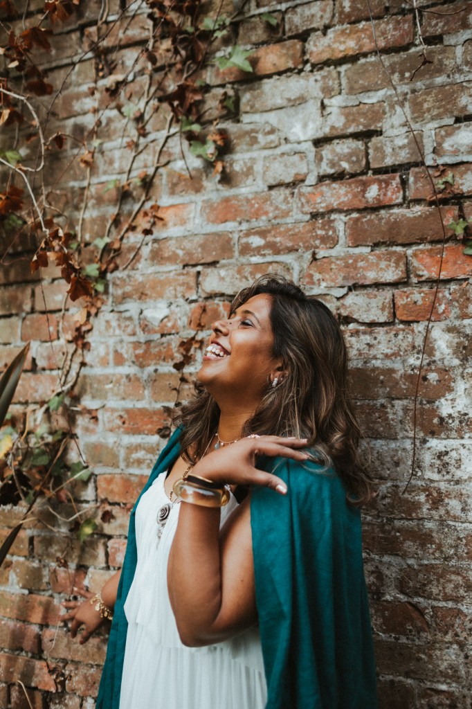 Nisha smiling standing in front of a brick wall.