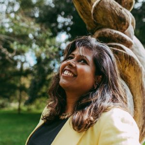 Nisha leaning against a tree in the park.