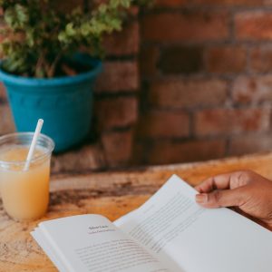 A person, Nisha, holds a book. A drink is visible on the table to her left.