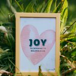 A "Joy is choosing to believe in me" postcard lying in the grass.