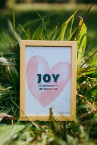 A "Joy is choosing to believe in me" postcard lying in the grass.
